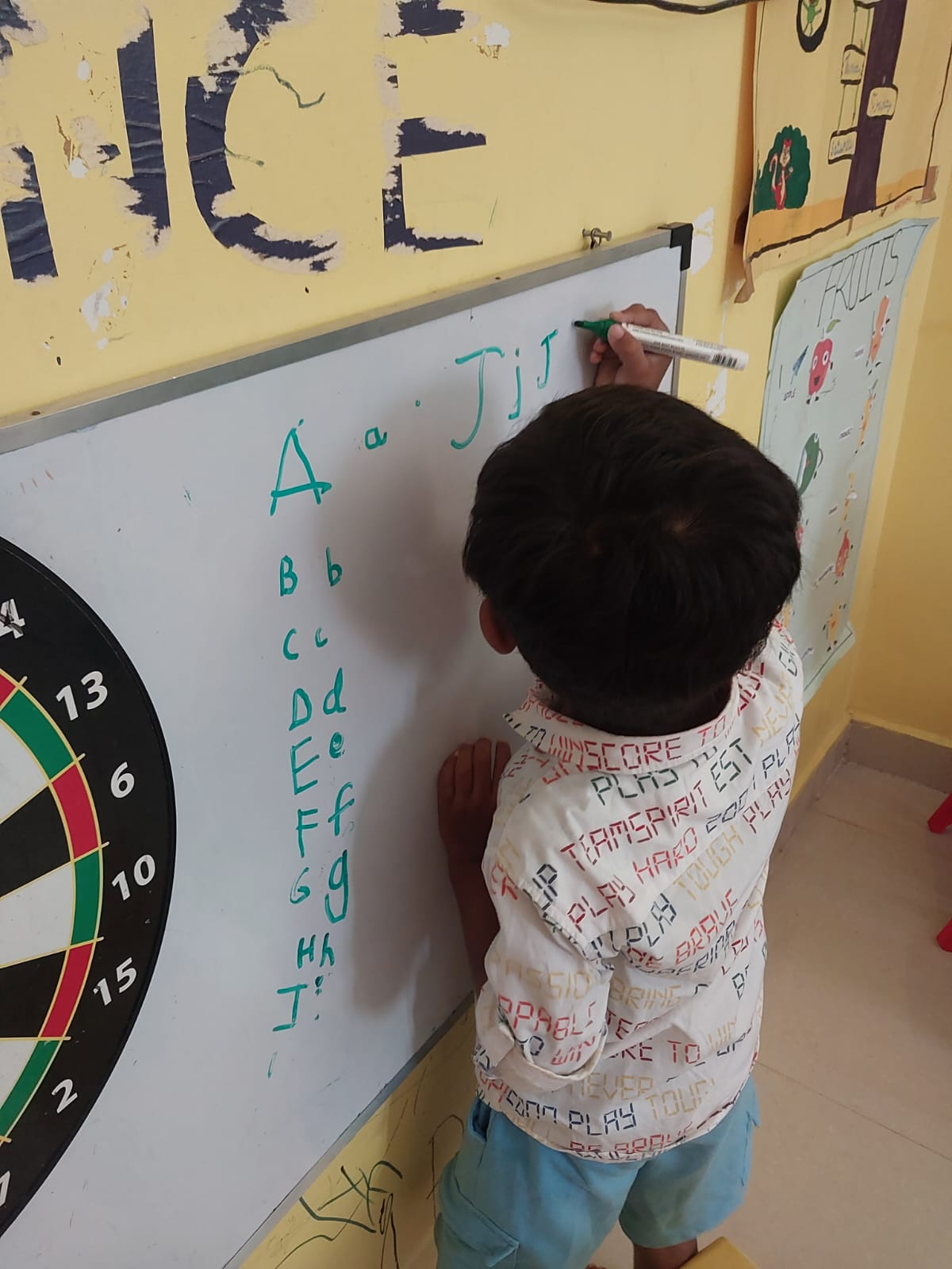 Child writing alphabet letters A to J on a whiteboard